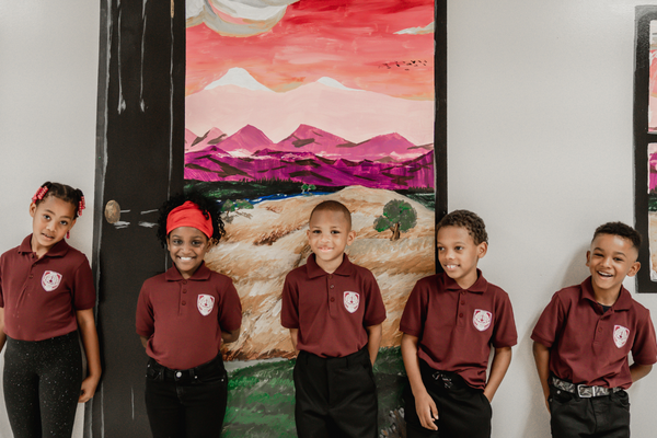 Five PACE Academy scholars in burgundy shirts and black pants stand in front of large mountain landscape painting.