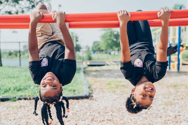 Two PACE Academy students pose upside down on playground equipment outside.