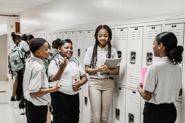 PACE Academy scholars gather around lockers holding books and talking to one another.