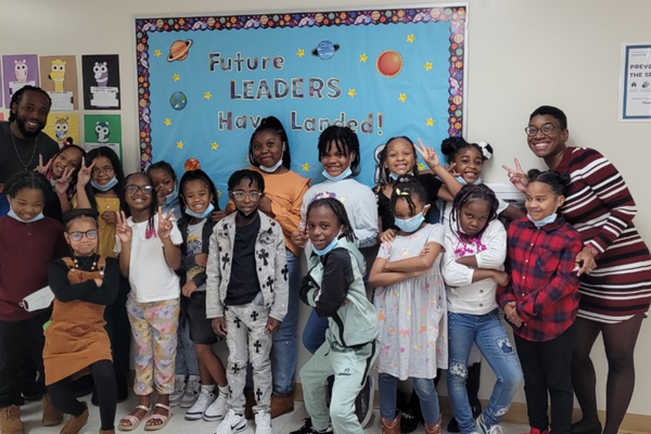 PACE Academy teacher, Mrs. Smith smiles and poses with her third grade class in front of an outer space bulletin board that says, “Future leaders have landed”.