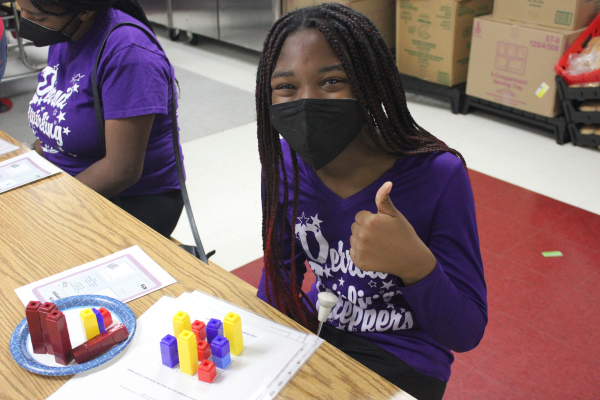 PACE Academy student in purple Detroit Twirling Steppers shirt, gives a thumbs up at a table where they have colorful stacks of cubes arranged on a form in front of them.