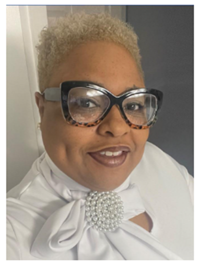 PACE Academy Principal Timeka Brown poses for camera in tortoiseshell glasses wearing a white blouse with pearl brooch