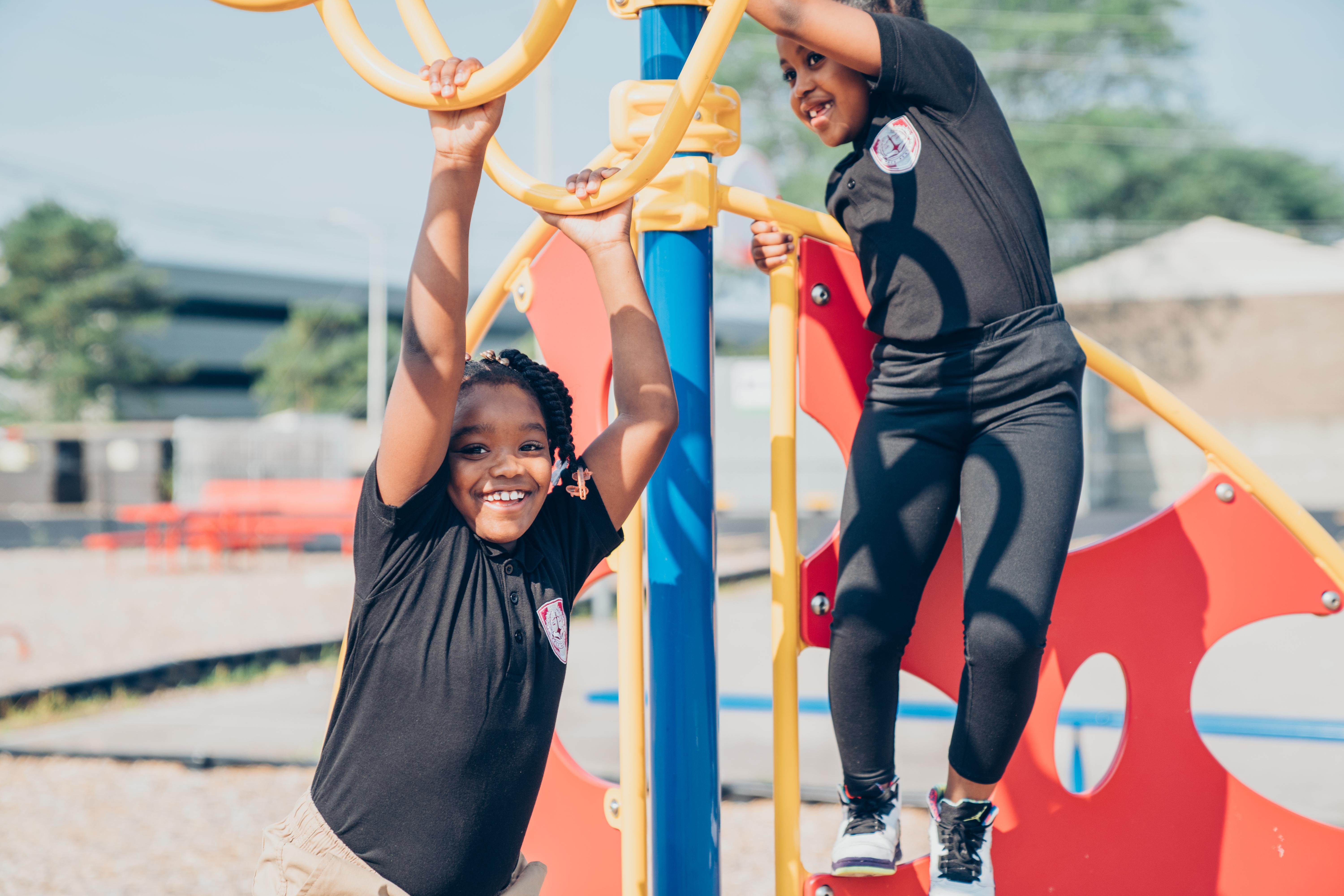 Two PACE Academy students smile while on a colorful play structure on campus.